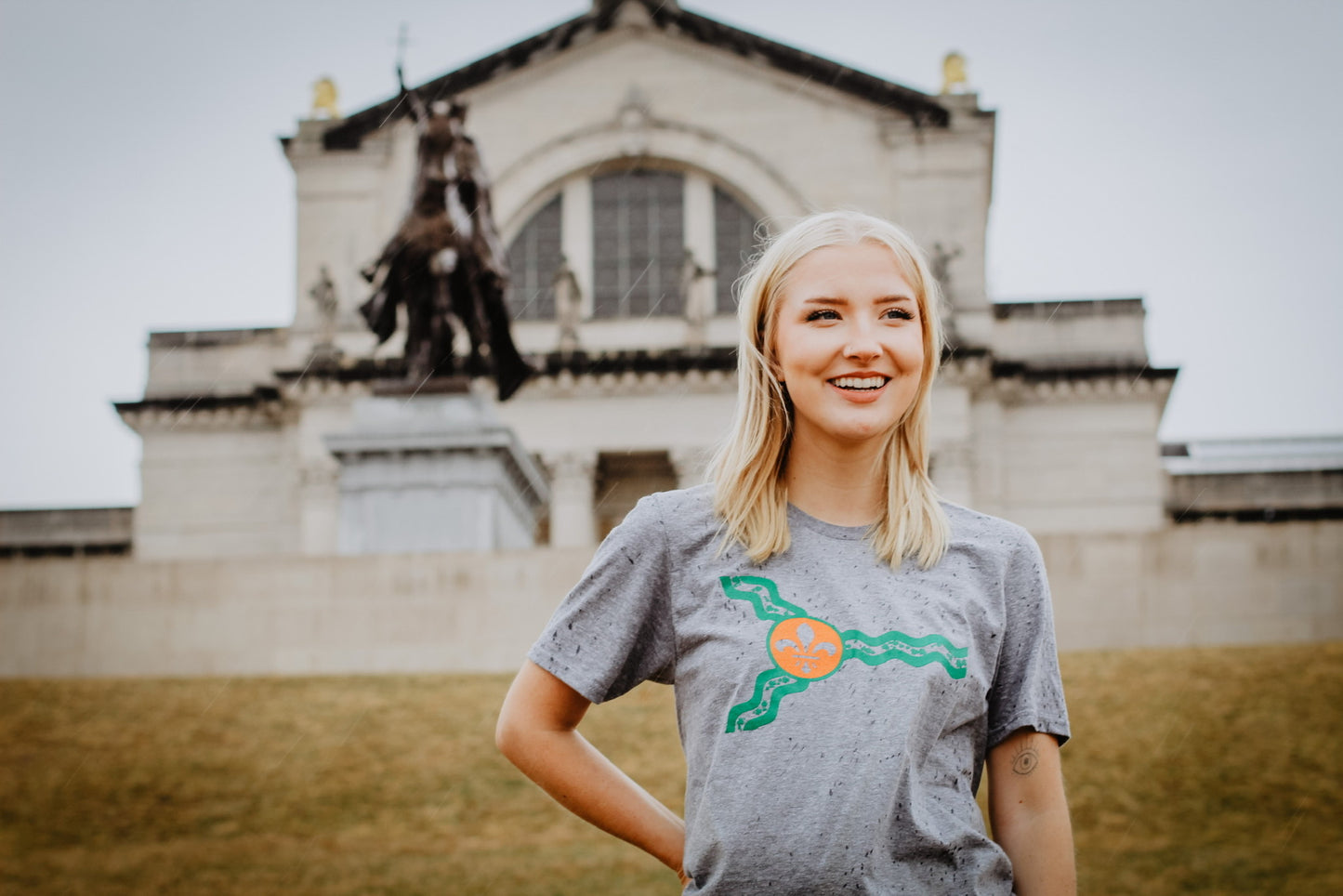 A woman wearing a grey St. Louis flag St. Patrick's day shirt in front of the St. Louis Art Museum.