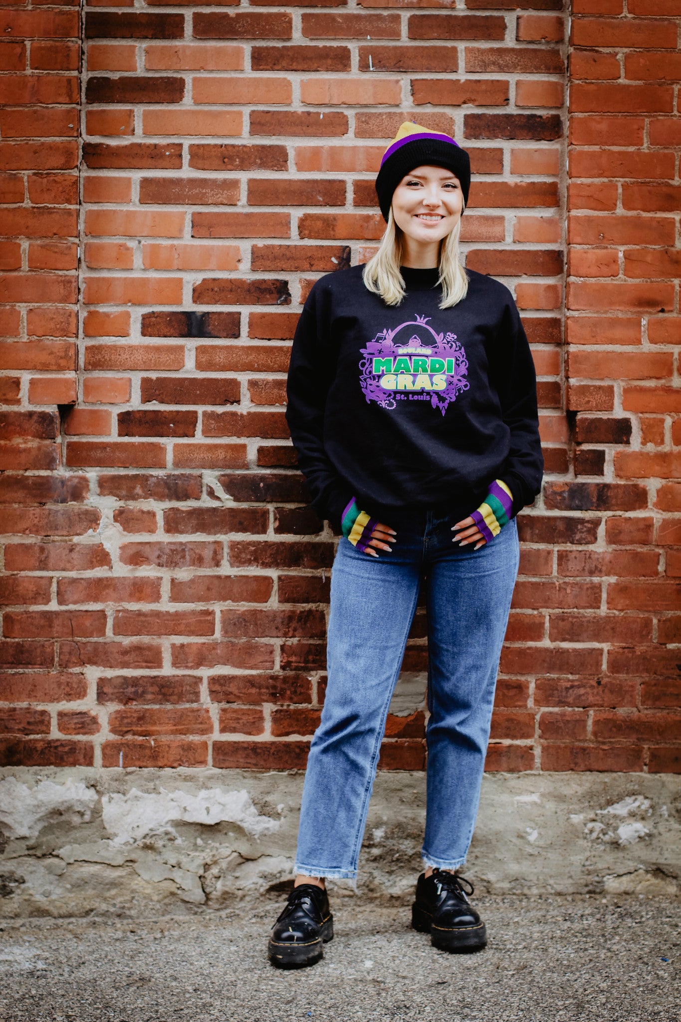 A woman wearing Soulard Mardi Gras clothing and accessories standing in front of a brick wall.