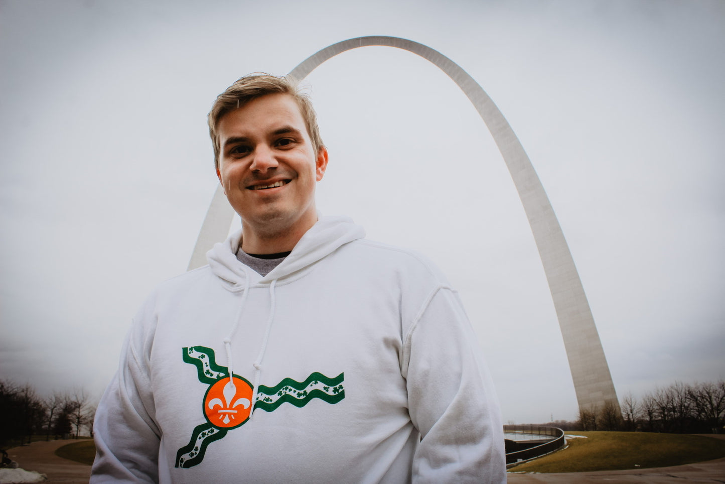 A man wearing the white St. Louis St. Patrick's Day hoodie while standing in front of the Arch.