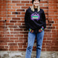 A woman wearing Soulard Mardi Gras clothing and accessories standing in front of a brick wall. 